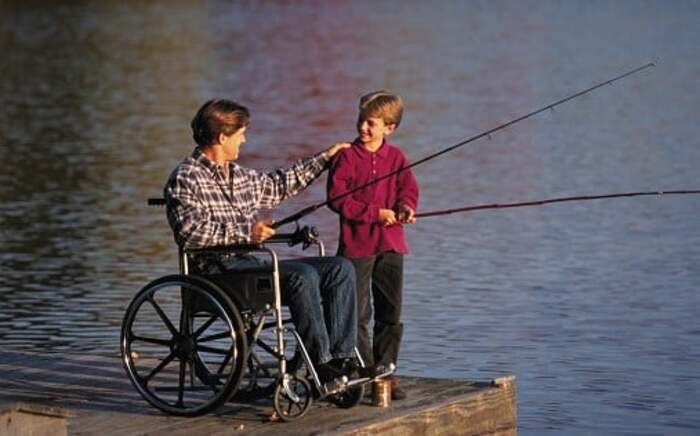 un homme en fauteuil et un enfant pêchant sur un ponton au bord de l'eau