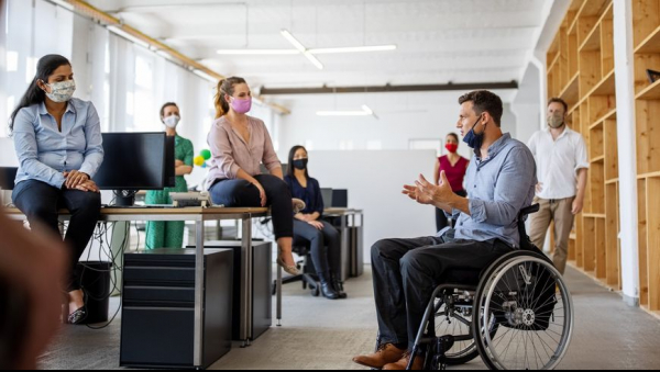 Homme en fauteuil discutant avec des collègues dans un bureau