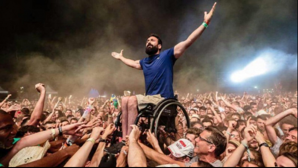 Homme en fauteuil porté par la foule lors d'un spectacle